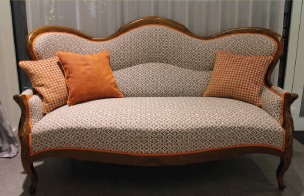 Aufgearbeitetes Biedermeier-Sofa mit hellem Musterstoff und orangefarbenen Kissen.