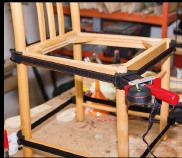 Freigelegtes Stuhlgestell in der Werkstatt, mit Spanngurten fixiert.